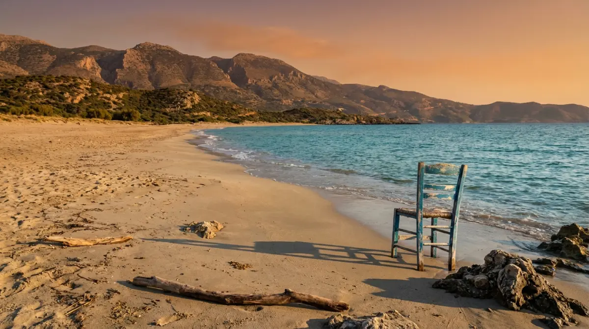 Pusta plaża na Krecie jesienią: samotne krzesło nad brzegiem morza, w oddali góry i miękkie, popołudniowe słońce.