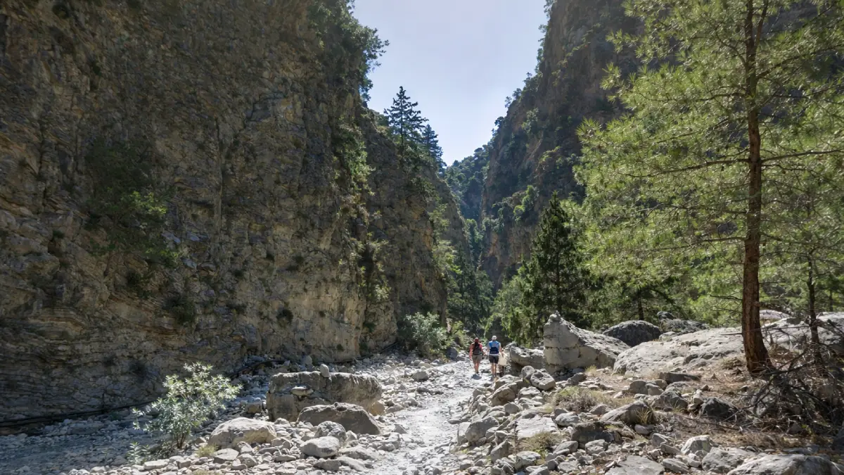 Trasa piesza przez Wąwóz Samaria na Krecie: wąska ścieżka dnem kanionu otoczona przez monumentalne wapienne ściany skalne i rzadką roślinność Gór Białych.
